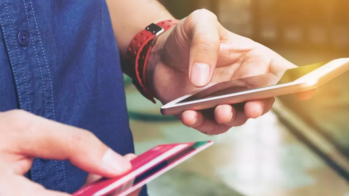 Pessoa segurando um cartão de crédito para fazer um pagamento no celular